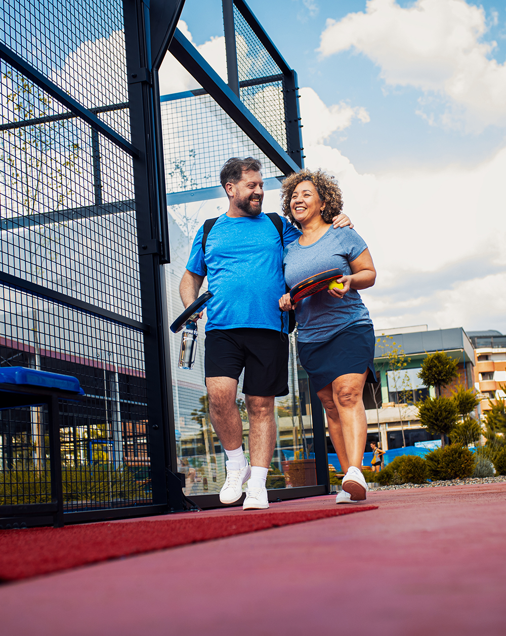 Smiling mix couple comes to the outdoor court to play padel.